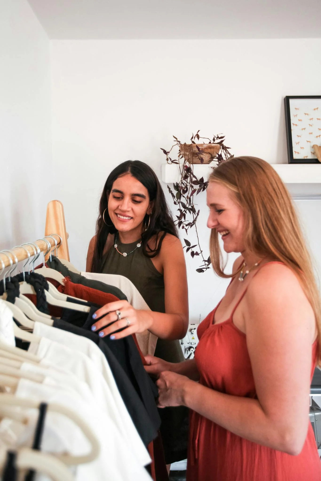 Two women enjoying shopping together in a cozy boutique setting, selecting clothes from a rack.