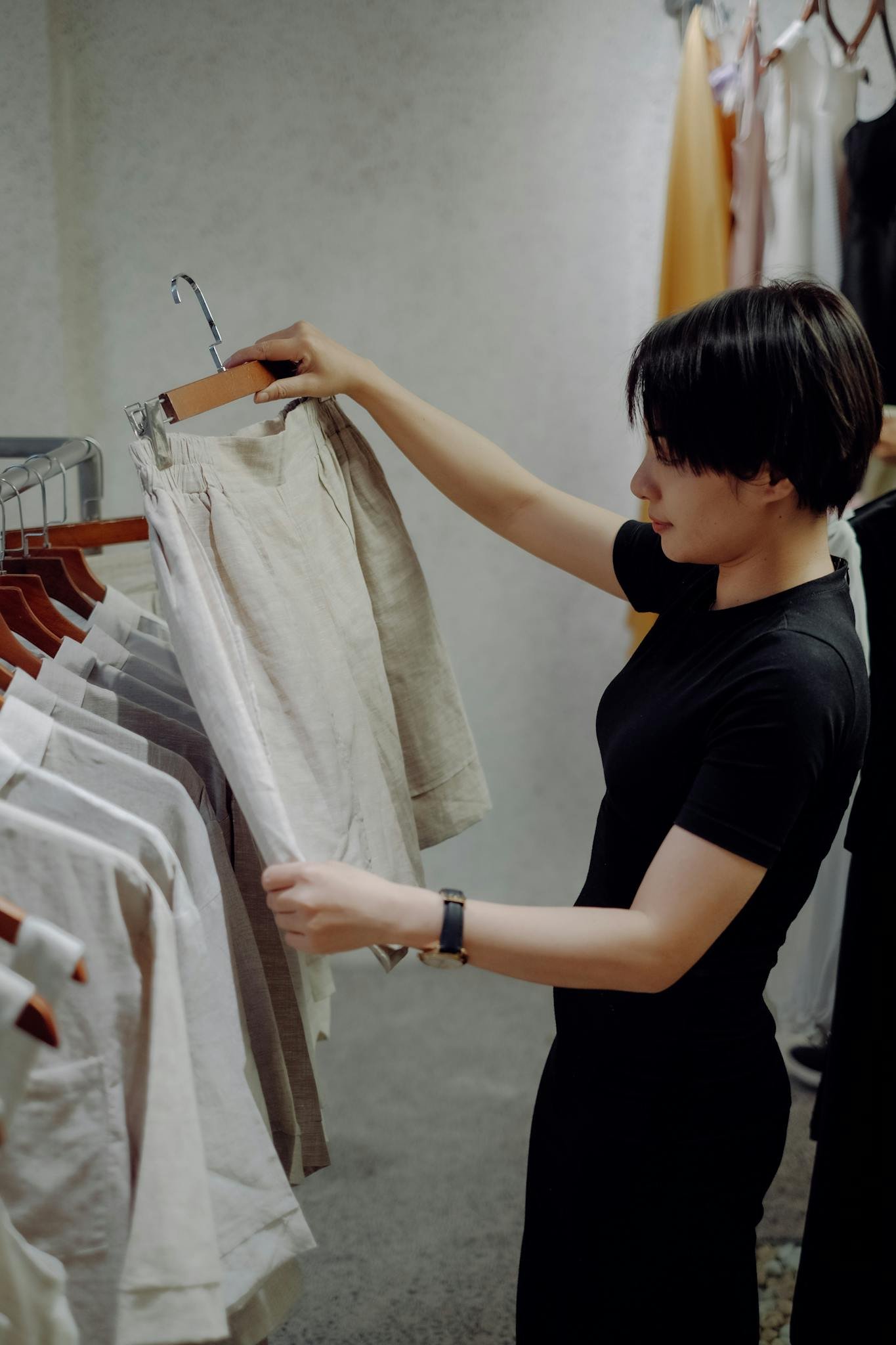 Young woman examines clothes in a minimalist fashion store, focused on a pair of beige shorts.
